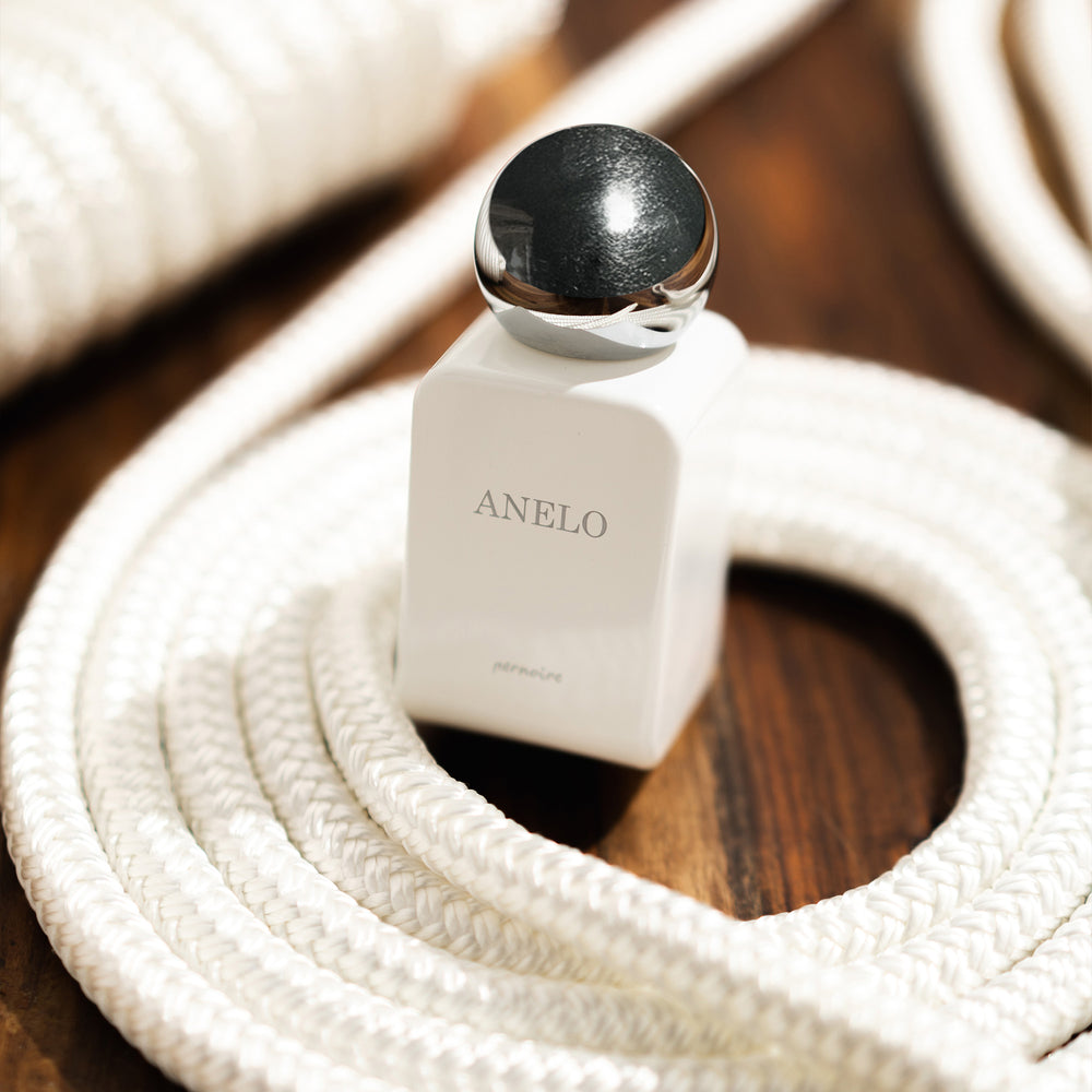 Pernoire Anelo parfumflacon tussen opgerold wit touw op een houten ondergrond