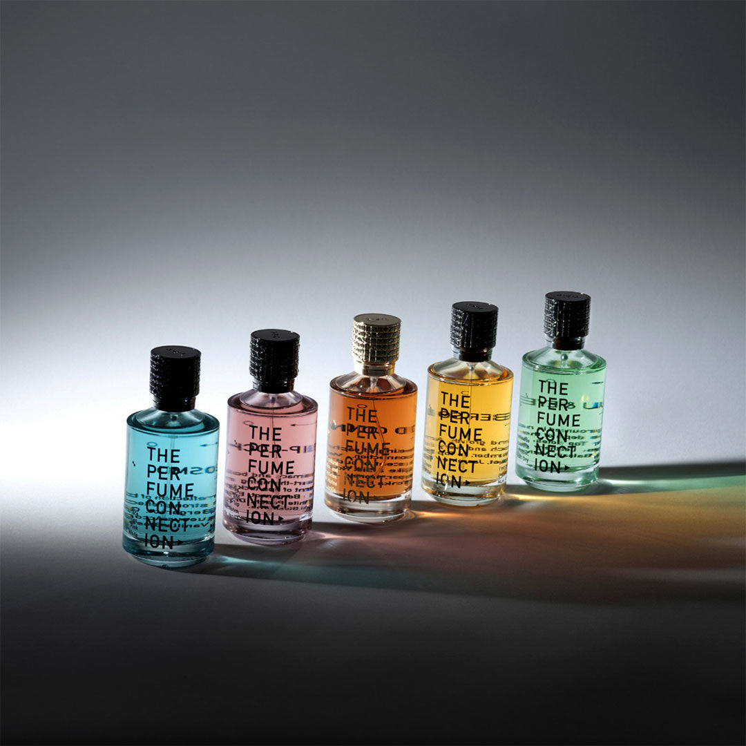 Collectie van vijf kleurrijke parfumflesjes van The Perfume Connection in een elegante opstelling tegen een grijze achtergrond.